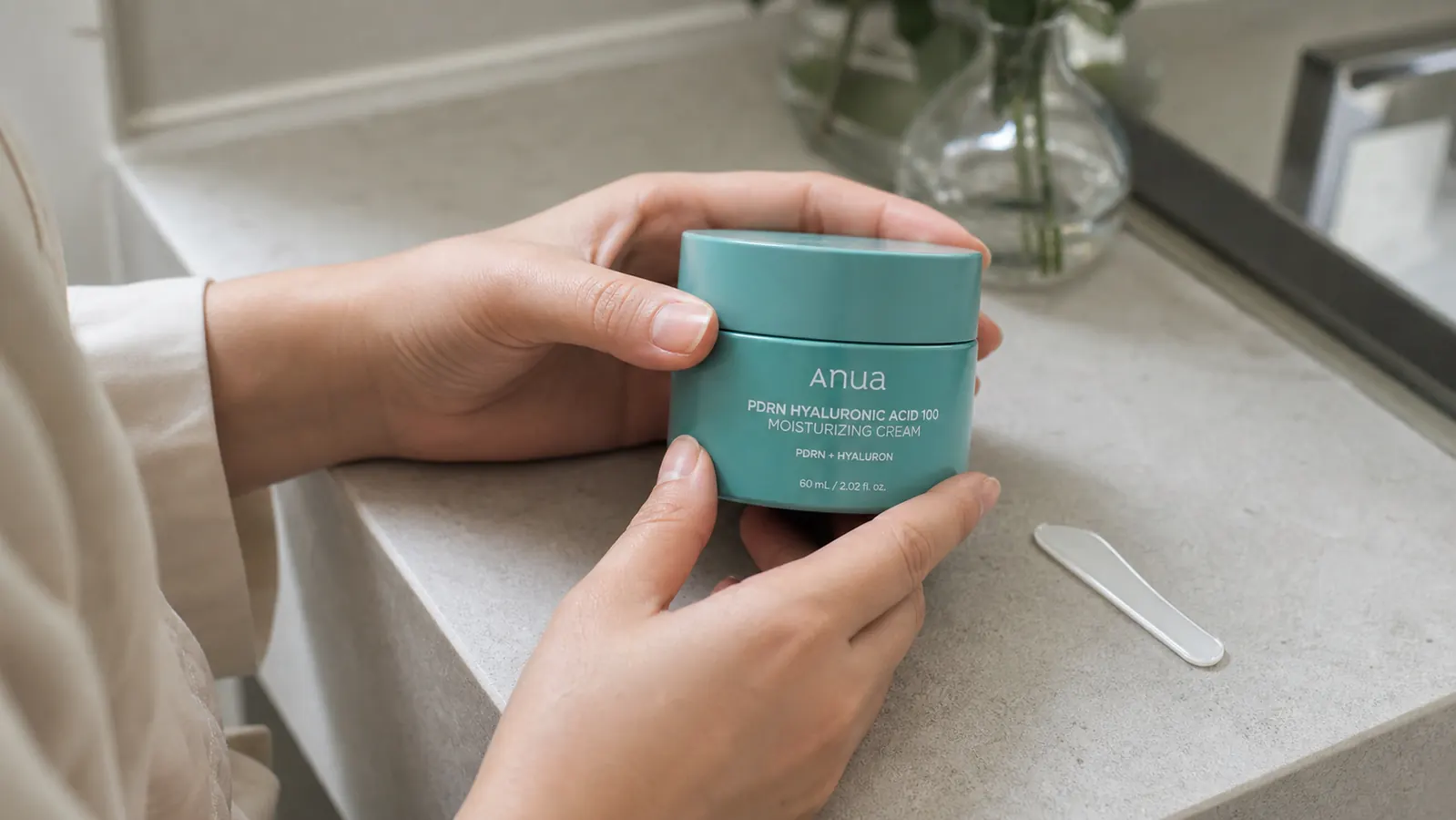 Close-up of the Anua PDRN cream being applied to the back of a hand showing its gel-cream texture