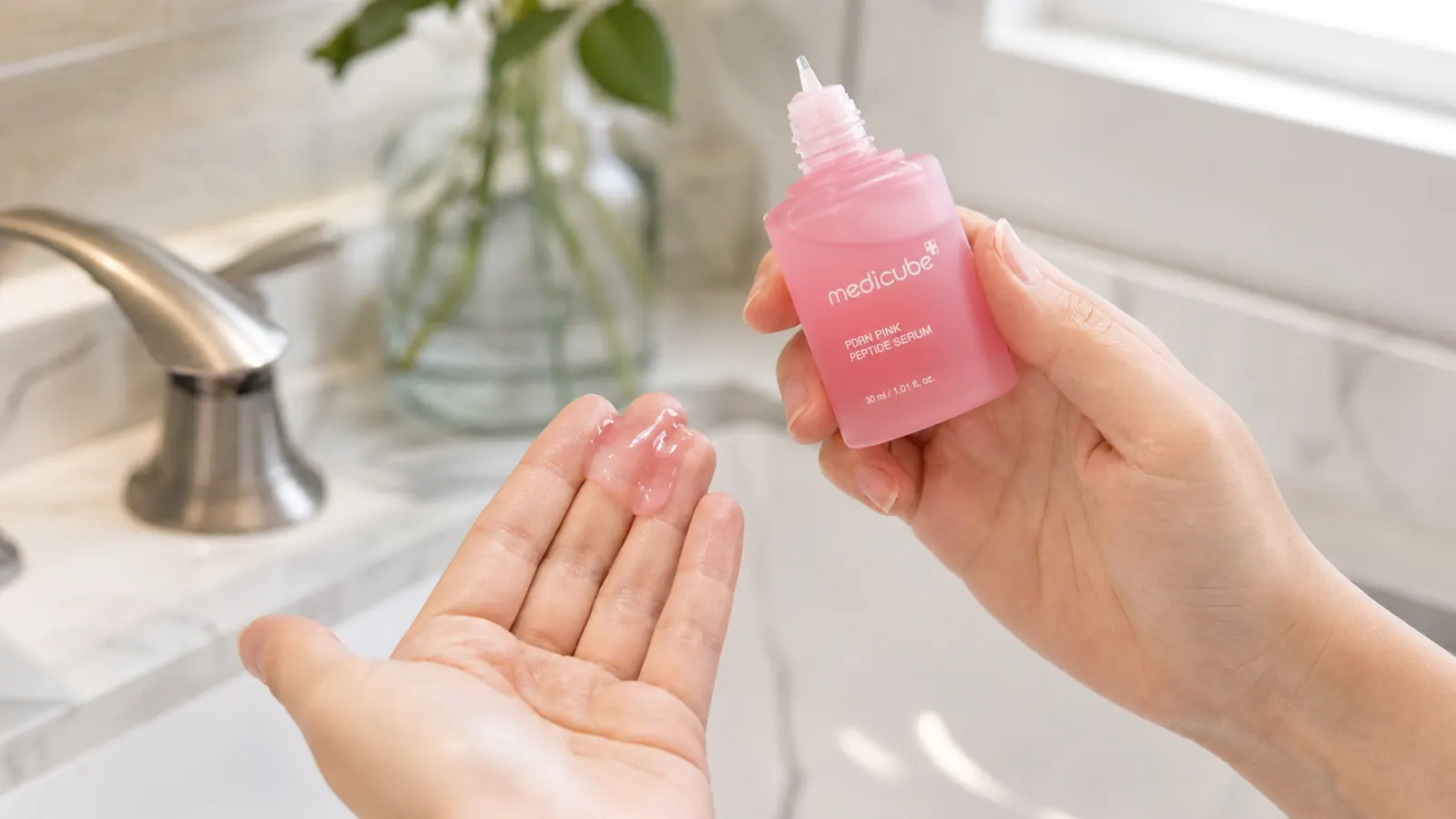 Close-up of the medicube PDRN Pink Peptide Serum bottle being held over a bathroom sink, dropper visible