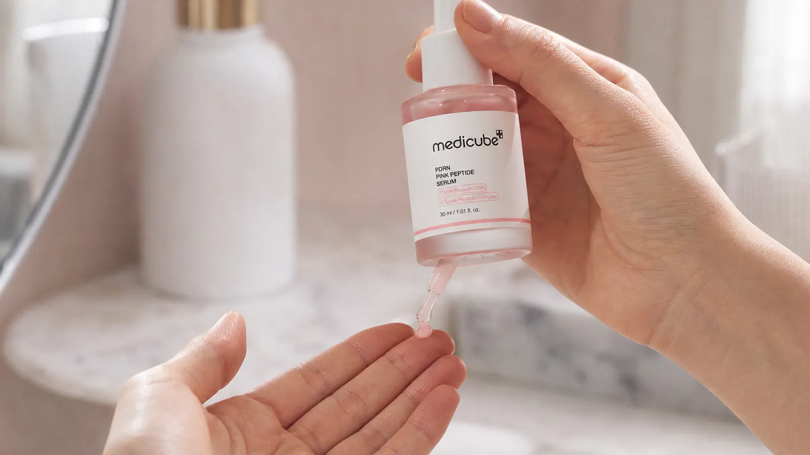 Close-up of a hand pressing the dropper applicator of the medicube PDRN Pink Peptide Serum, dispensing a pale pink drop onto fingertips
